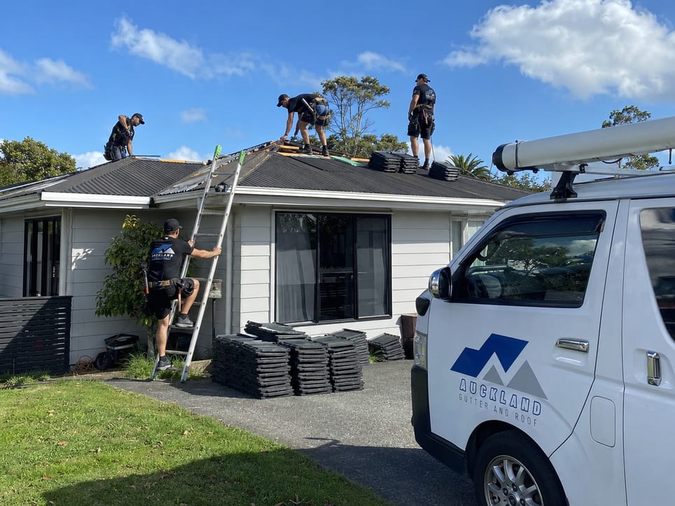Four Auckland Gutter and Roof staff working on a single-storey roof beside their branded van