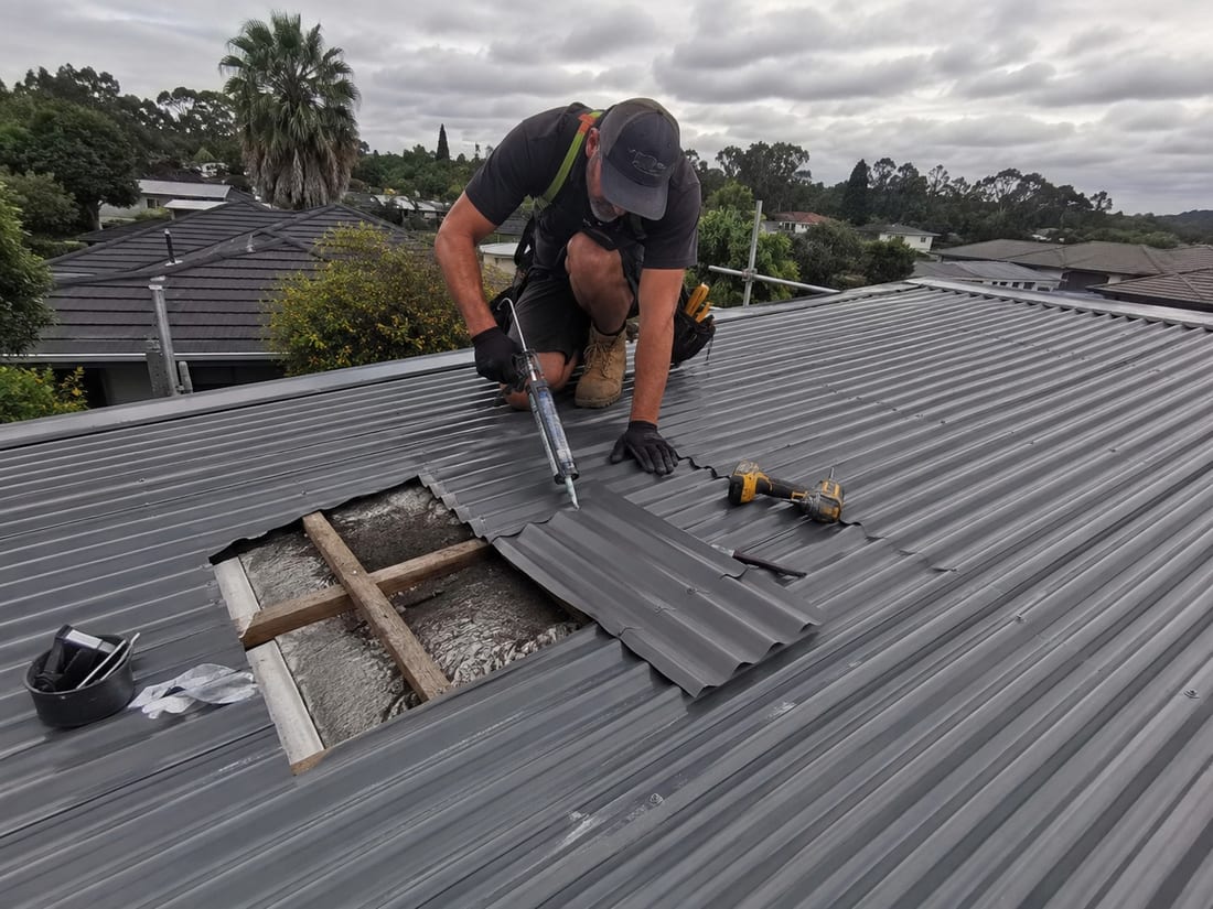 Harnessed roof leak repair contractor sealing a hole cut in a long-run steel roof in Auckland