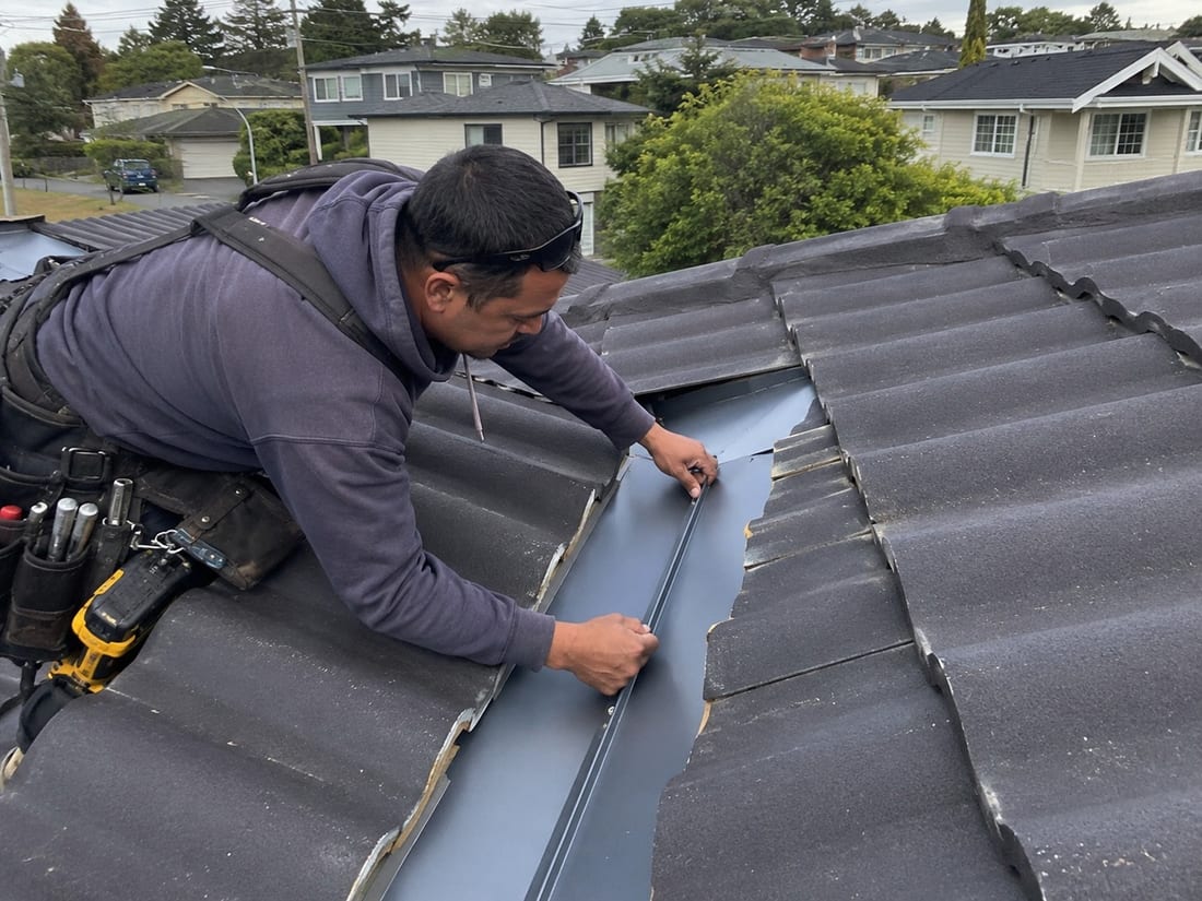 Roofer fixing a new valley flashing between two tiled sections of an Auckland roof