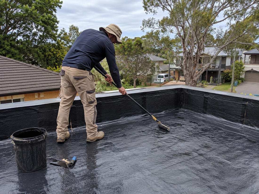 Roofer rolling black butynol coating across a flat roof and up the parapet on an Auckland home