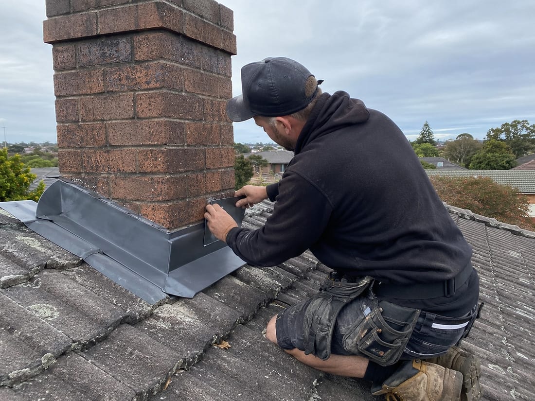 Roofer fitting new chimney flashing around a brick chimney on an Auckland tile roof