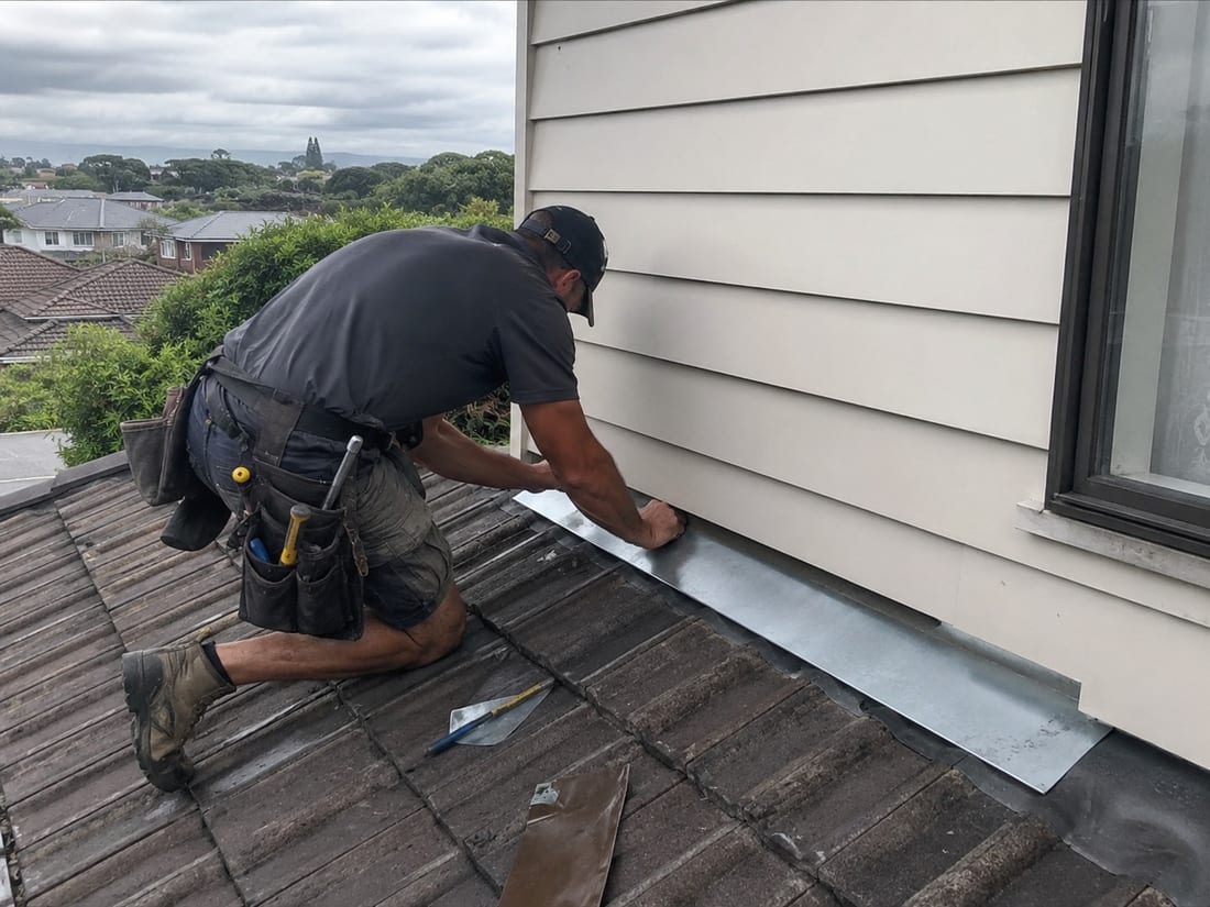 Roofer fitting a new apron flashing where an Auckland tile roof meets a weatherboard wall