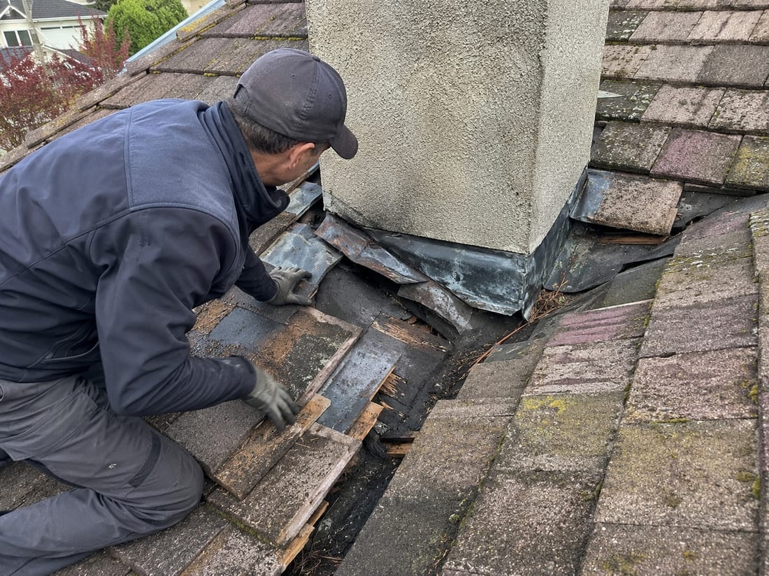 Roofer lifting tiles beside a chimney on an Auckland roof to reach the leaking flashing underneath